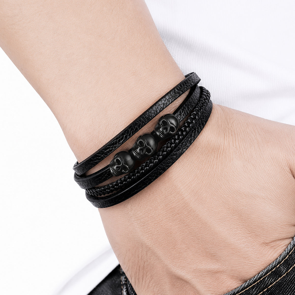 Svart läderarmband med olika strukturer, smyckat med tre detaljerade dödskallar