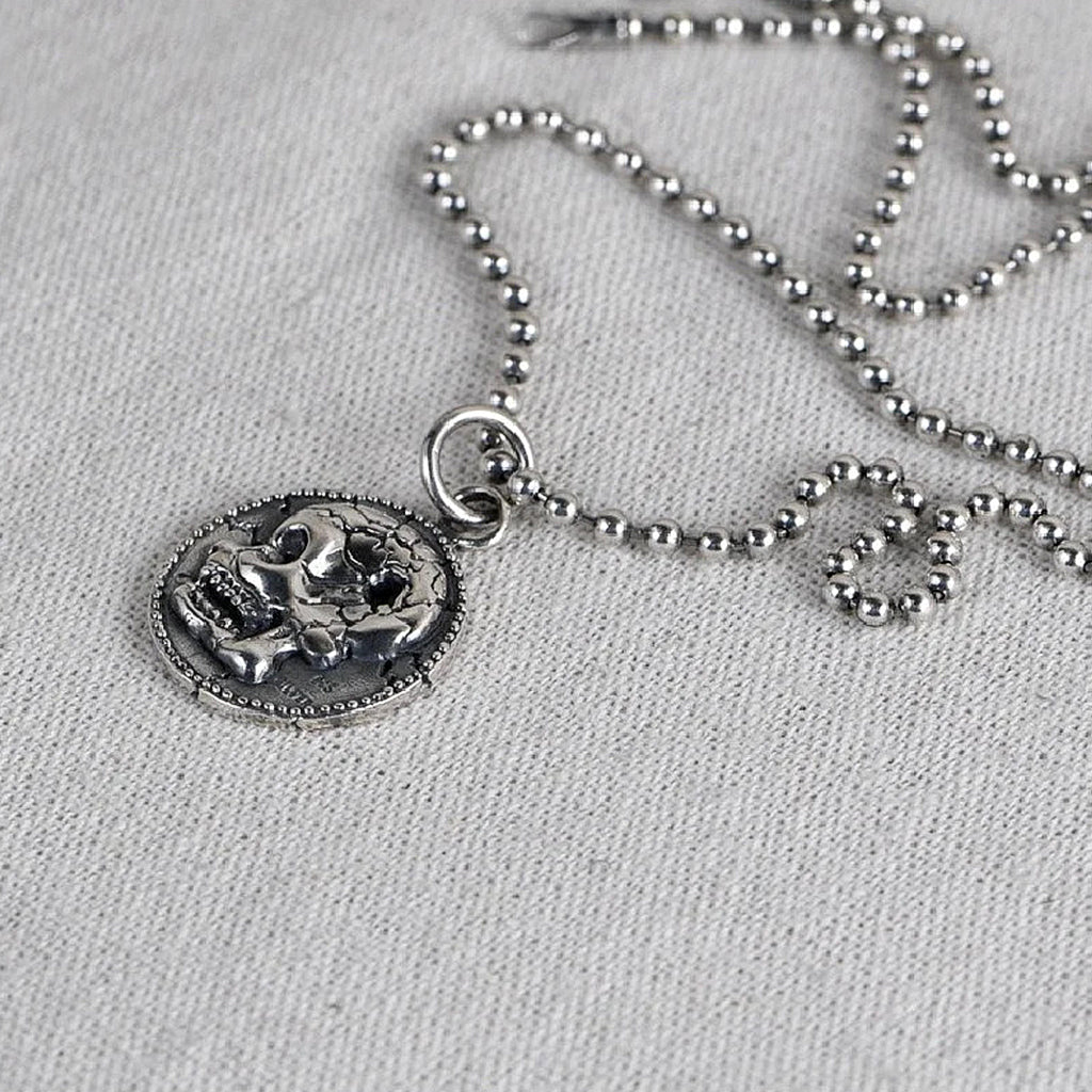 Smycke av sterlingsilver föreställande ett cirkelformat mynt avbildande en dödskalle med ett kulhål i skallen