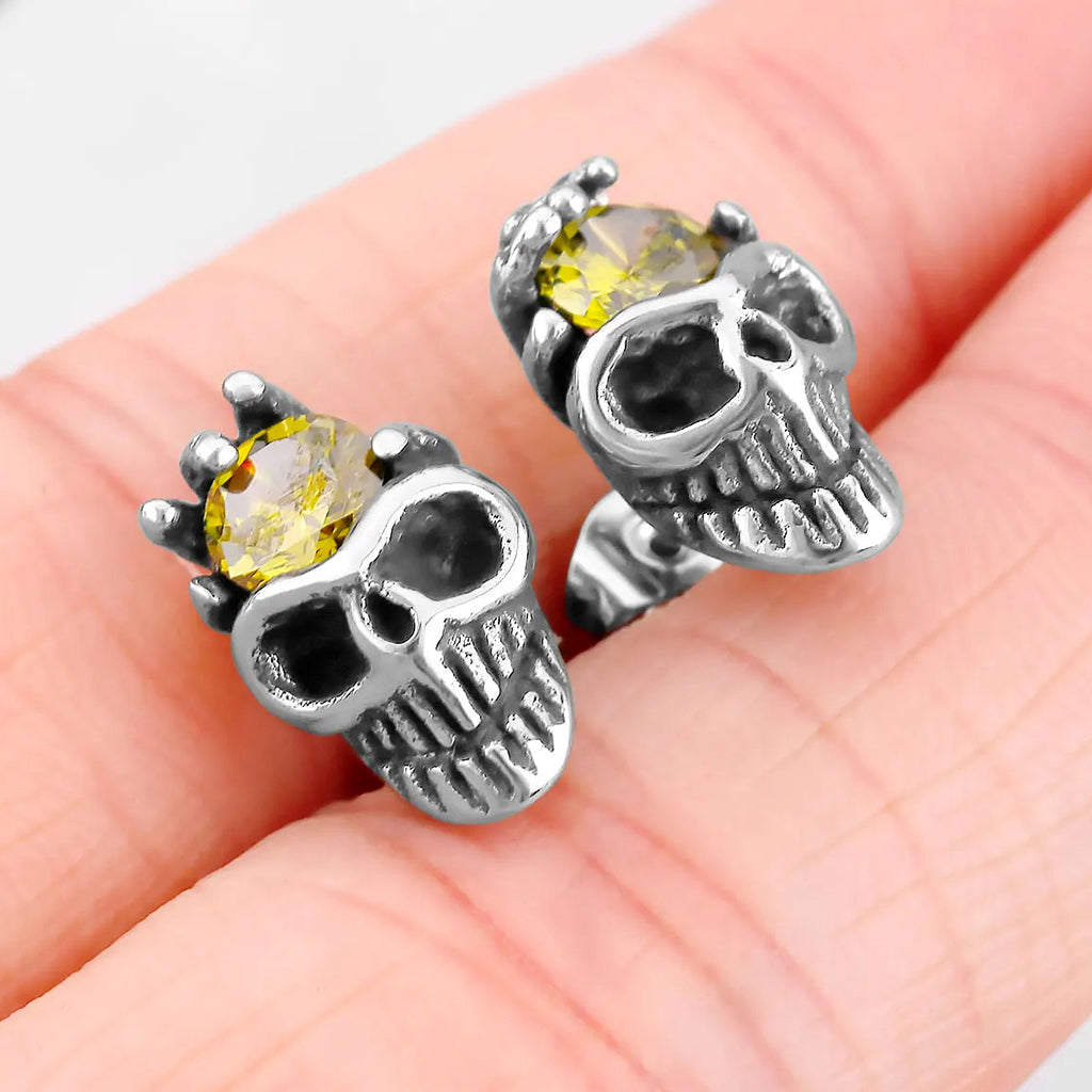 Silverfärgad ear stud som visar en dödskalle med en skeletthand hållande en gul zirkon