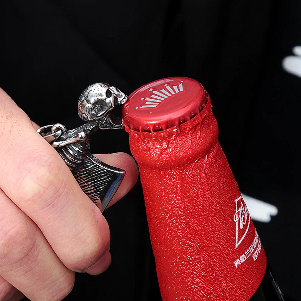 Silverfärgat hängsmycke föreställande en liten slaktkniv med en gapande döskalle, som fungerar som kapsylöppnare