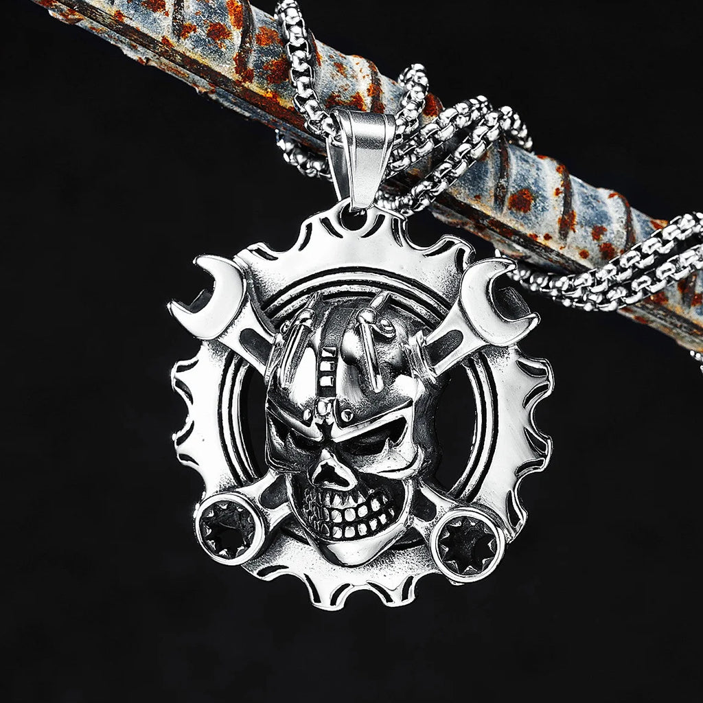 Silverfärgat hängsmycke föreställande ett kugghjul med ett kranium med korslagda skiftnycklar