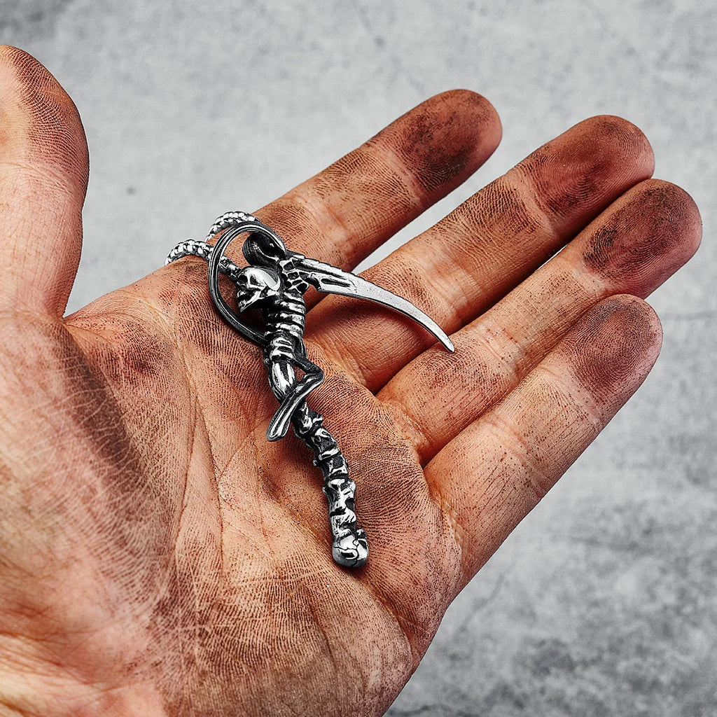 Silverfärgat hängsmycke föreställande en lie med dödskallar