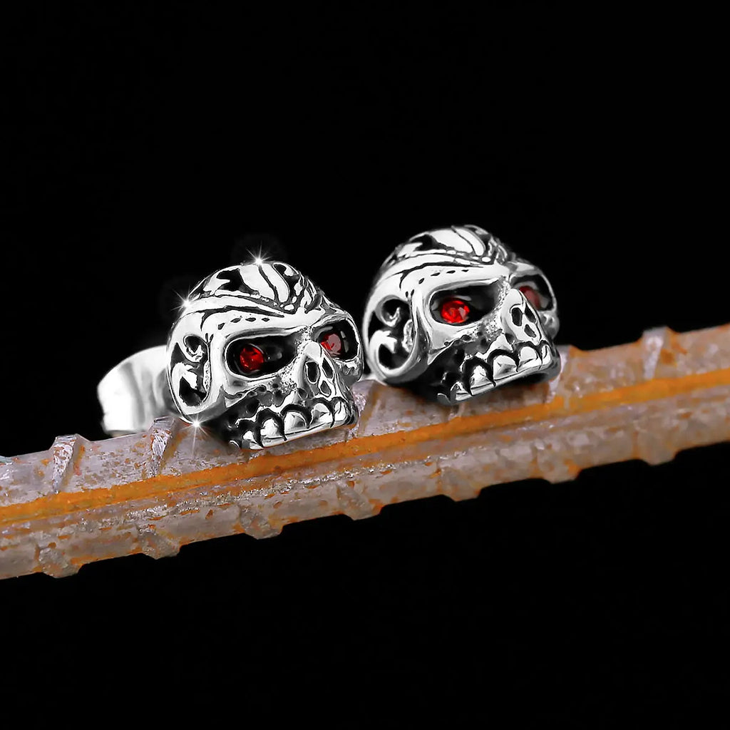 Silverfärgade örhängen som föreställer dödskallar med ornament och röda zirkoner som ögon