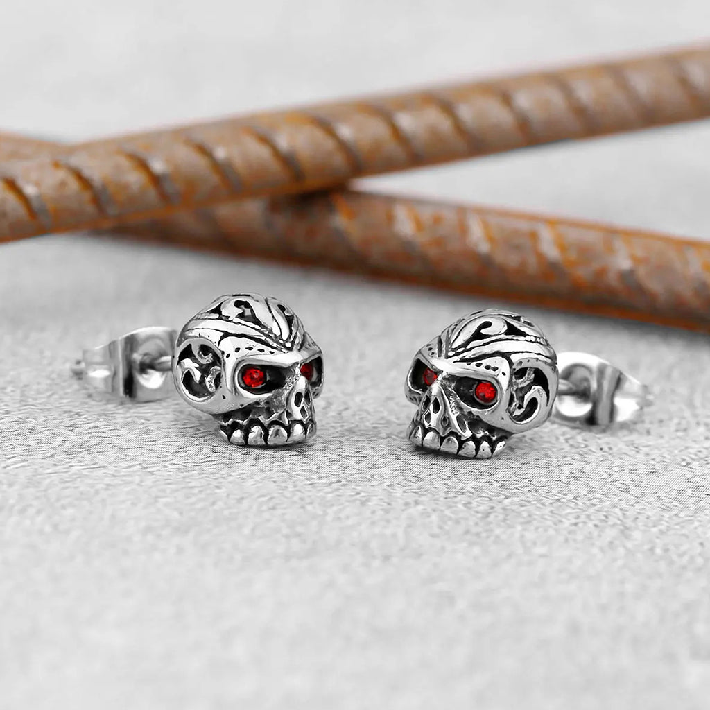 Silverfärgade öronstift som föreställer dödskallar med ornament och röda zirkoner som ögon