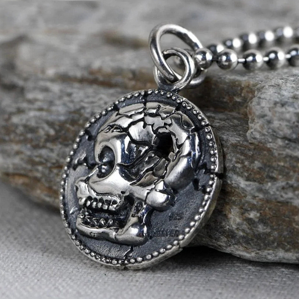 Smycke av sterling silver föreställande ett runt mynt avbildande en dödskalle med ett kulhål i skallen