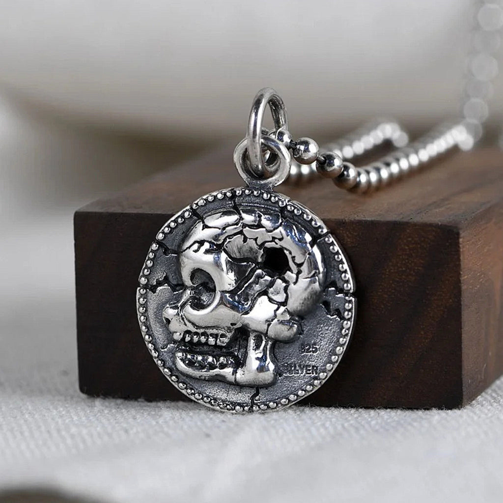 Smycke av sterling silver föreställande ett cirkelformat mynt avbildande en dödskalle med ett kulhål i skallen