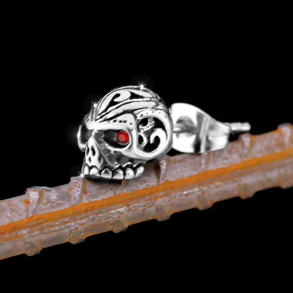 Silverfärgade stiftörhängen som föreställer dödskallar med ornament och röda zirkoner som ögon