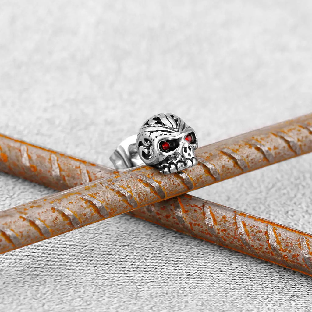Silverfärgade stud-örhängen som föreställer dödskallar med ornament och röda zirkoner som ögon