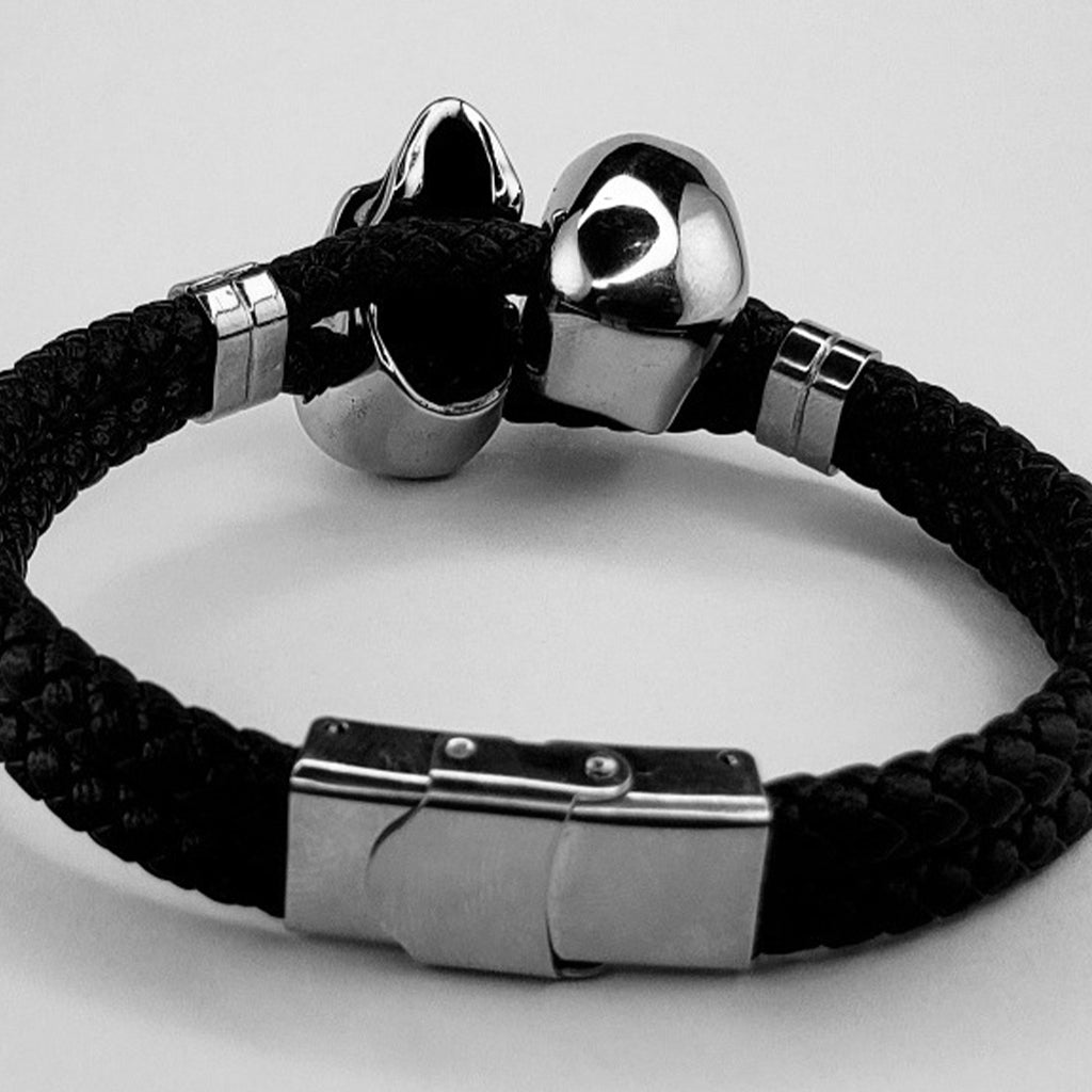Svart armband i flätat läder med två silverfärgade skallar i rostfritt stål