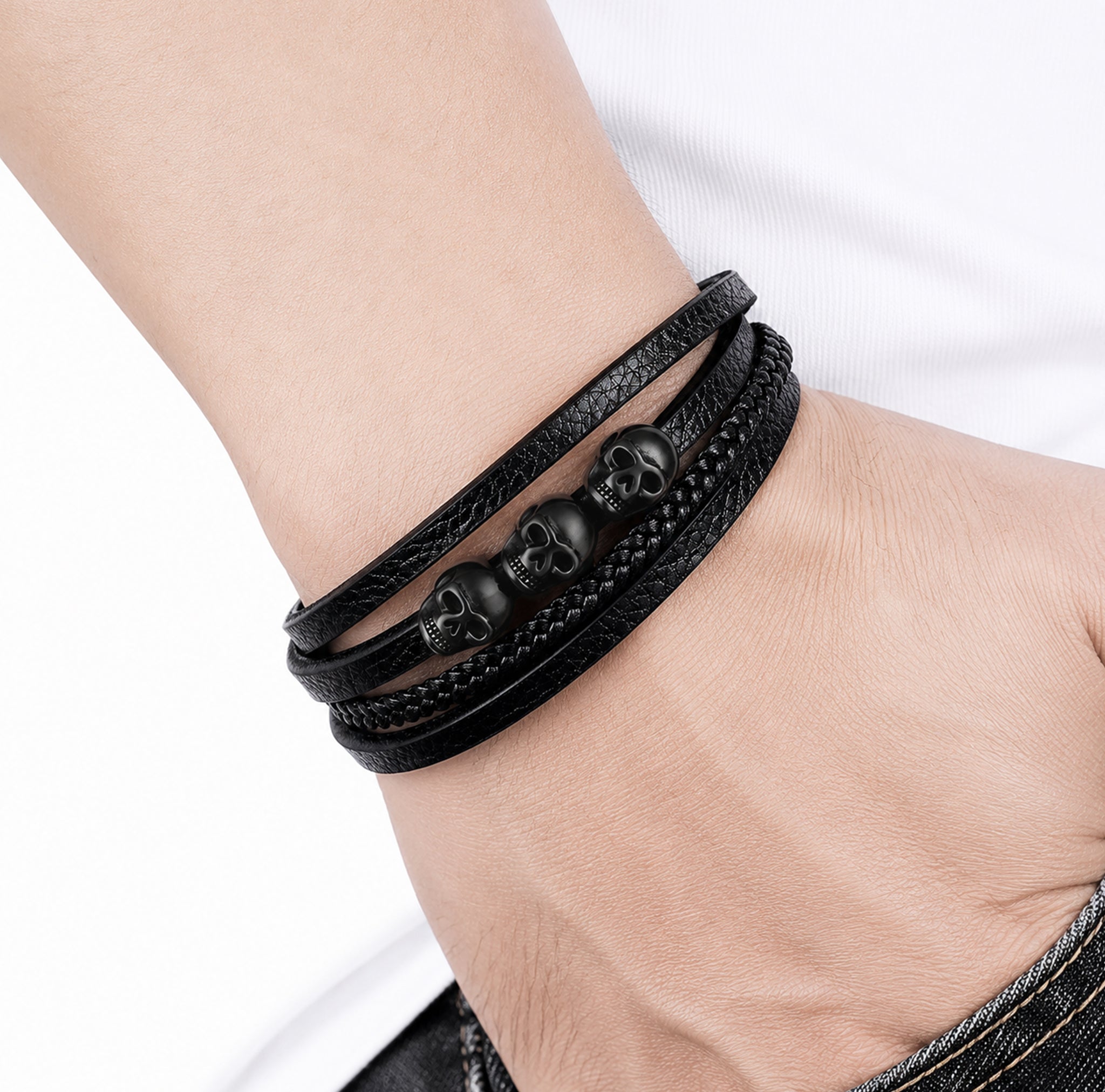 Svart läderarmband med olika strukturer, smyckat med tre detaljerade dödskallar