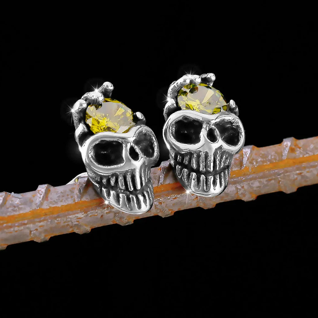 Silverfärgat örhänge som visar en dödskalle med en skeletthand hållande en gul zirkon