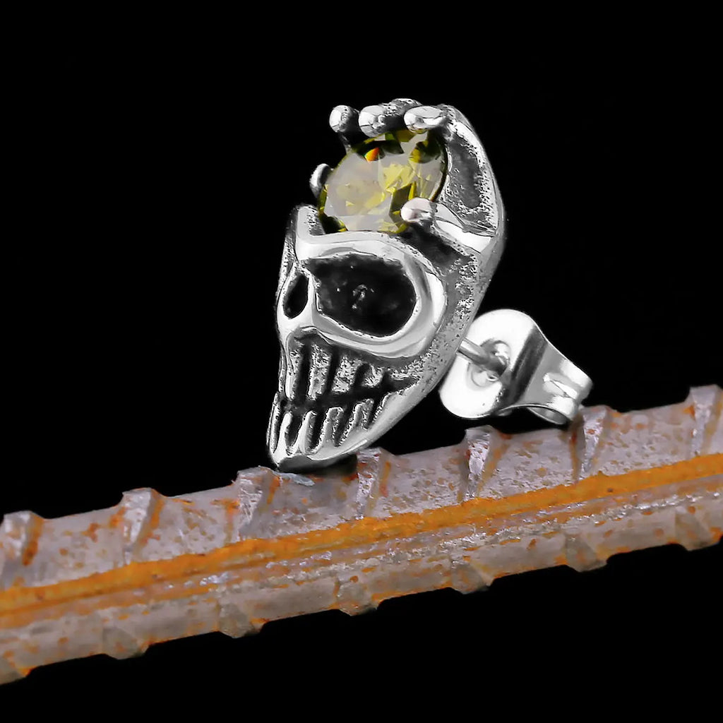 Silverfärgat öronstift som visar en dödskalle med en skeletthand hållande en gul zirkon