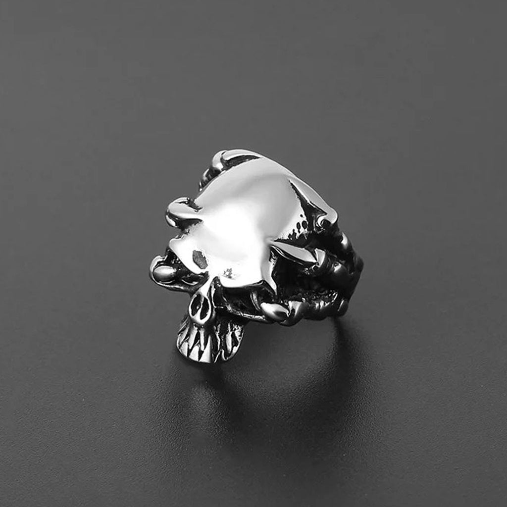 Silverfärgad ring av sterling silver föreställande en dödskalle som kramas av drakklor