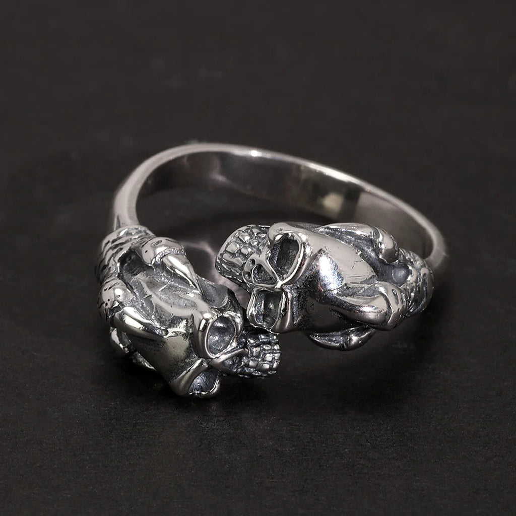 Silverfärgad ring av sterling silver föreställande två kranium som hålls fast av örnklor