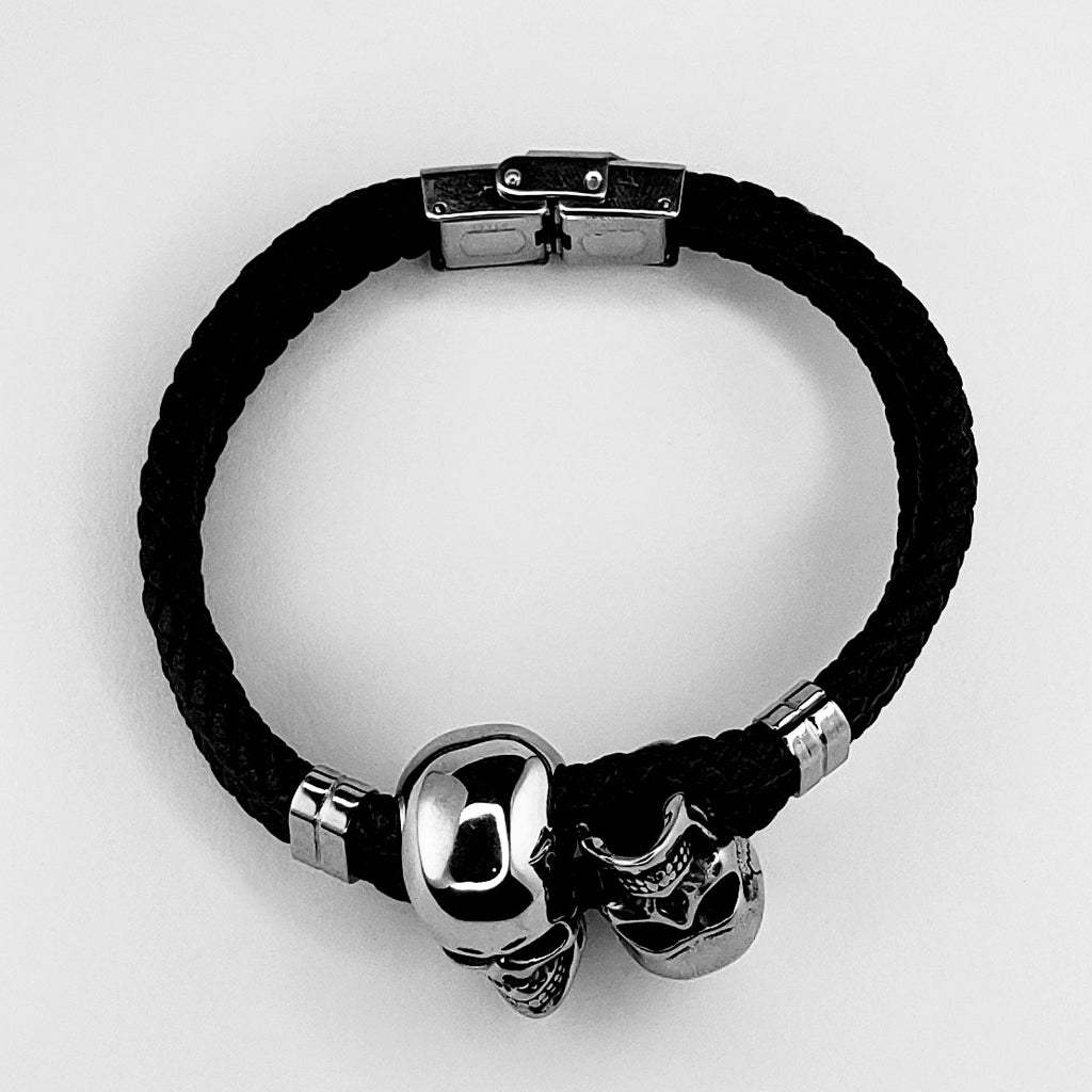 Svartfärgat armband i flätat läder med två silverfärgade dödskallar i rostfritt stål