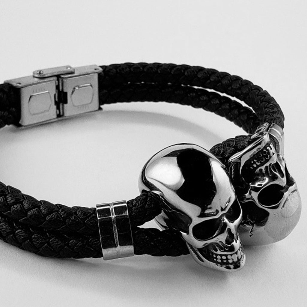 Mörkt armband i flätat läder med två silverfärgade kranium i rostfritt stål