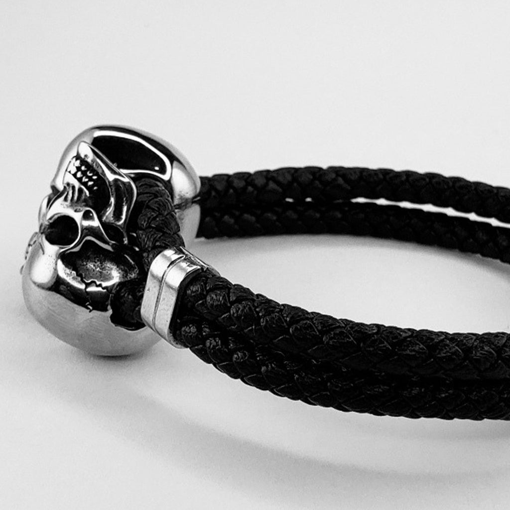 Mörkt armband i flätat läder med två silverfärgade skallar i rostfritt stål